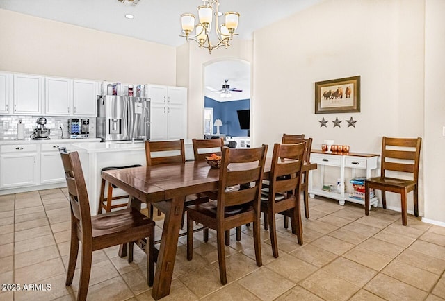 tiled dining room featuring ceiling fan with notable chandelier and a high ceiling