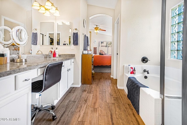 bathroom with a relaxing tiled tub, ceiling fan, wood-type flooring, and vanity