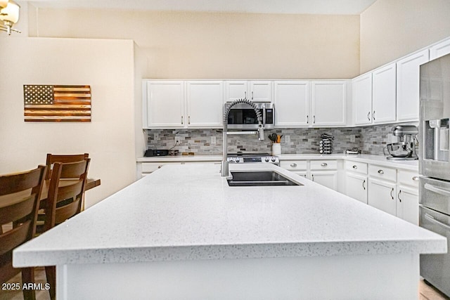 kitchen with tasteful backsplash, stainless steel appliances, an island with sink, and white cabinets