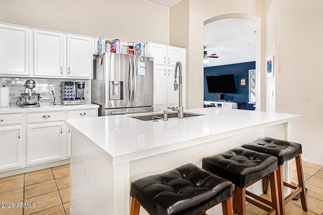 kitchen with a kitchen island with sink, light stone countertops, stainless steel fridge, and a kitchen breakfast bar