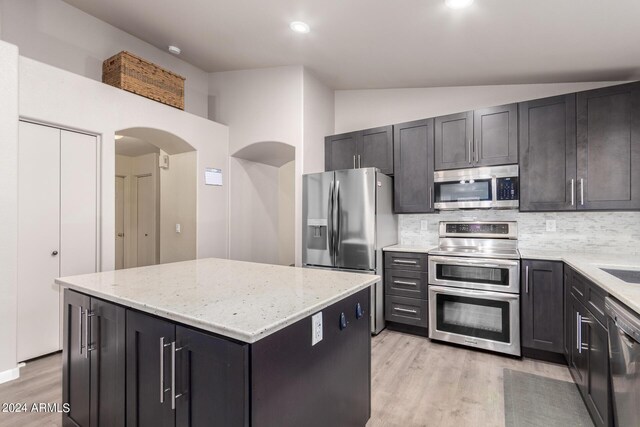 kitchen with appliances with stainless steel finishes, vaulted ceiling, a kitchen island, and light hardwood / wood-style flooring