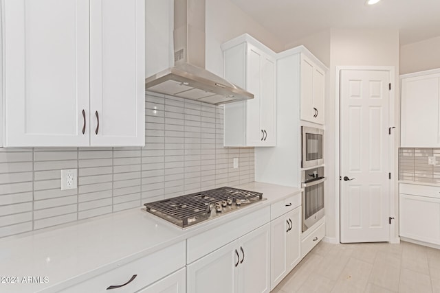 kitchen with wall chimney exhaust hood, appliances with stainless steel finishes, white cabinets, and tasteful backsplash