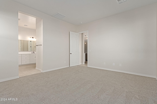 unfurnished bedroom featuring ensuite bathroom and light colored carpet