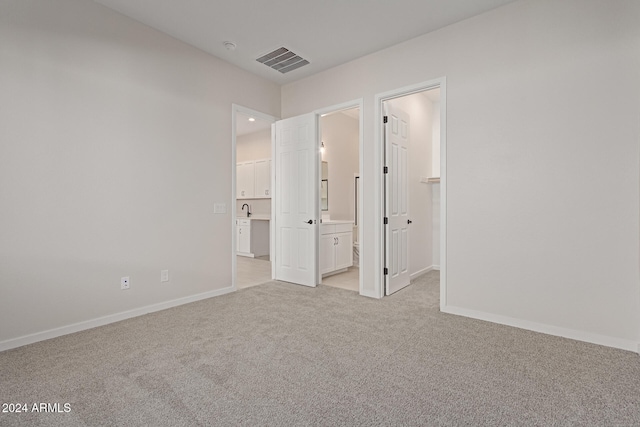 unfurnished bedroom with a spacious closet, ensuite bathroom, and light carpet