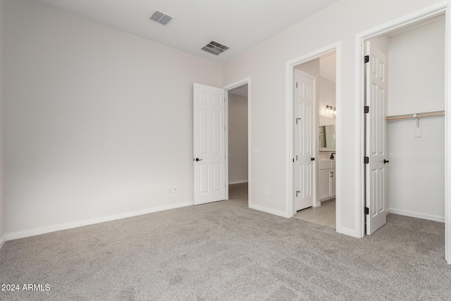 unfurnished bedroom featuring connected bathroom, a closet, a spacious closet, and light colored carpet