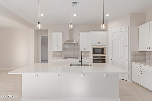 kitchen with stainless steel oven, a kitchen island with sink, hanging light fixtures, black microwave, and white cabinetry