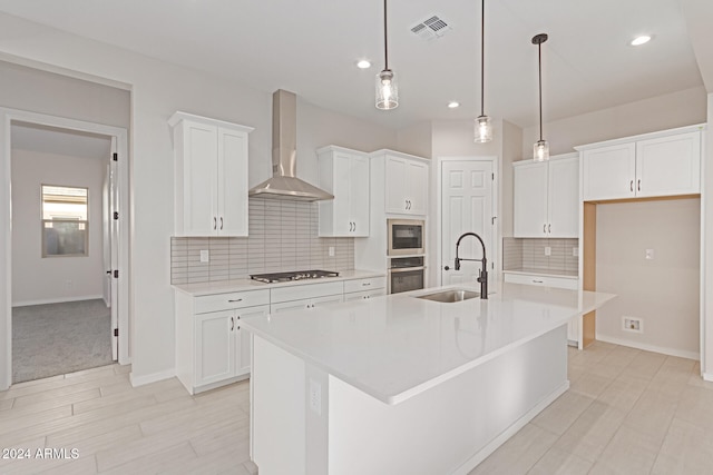 kitchen with wall chimney range hood, sink, a center island with sink, and white cabinets