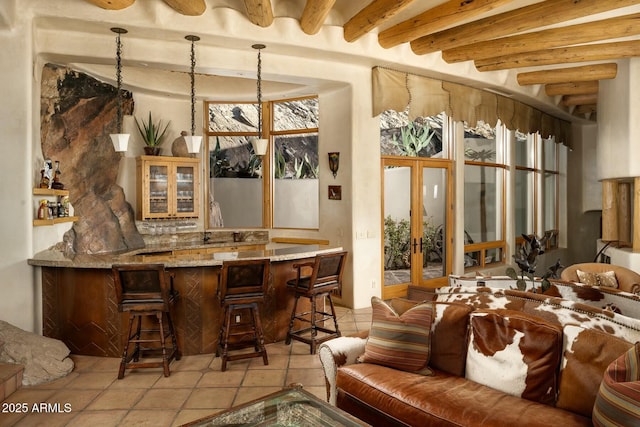 bar with beamed ceiling, light stone countertops, and pendant lighting