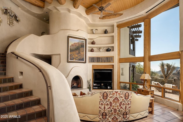 tiled living room with ceiling fan, wood ceiling, built in shelves, and beamed ceiling