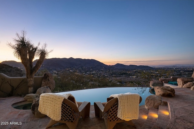 pool at dusk featuring a mountain view and a patio area