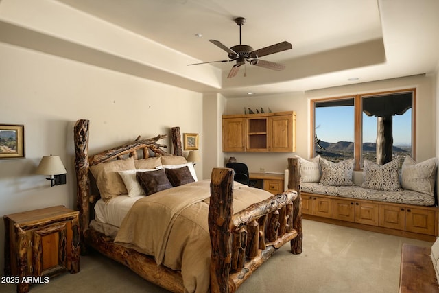 carpeted bedroom with a raised ceiling and ceiling fan