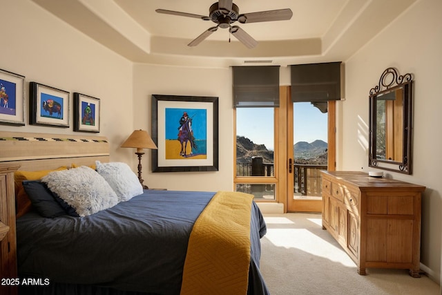 carpeted bedroom featuring a raised ceiling, a mountain view, access to outside, and ceiling fan