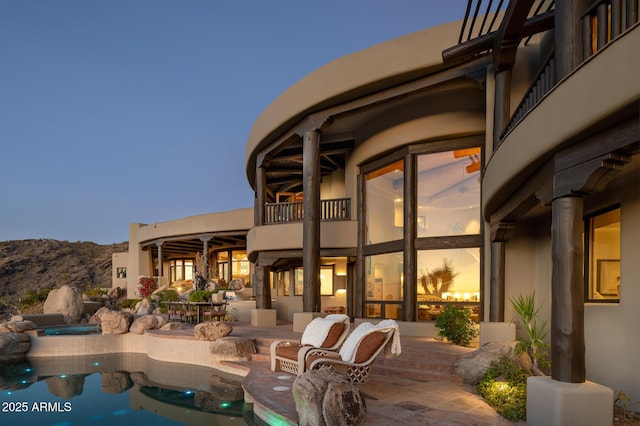 pool at dusk featuring an in ground hot tub, a mountain view, and a patio area