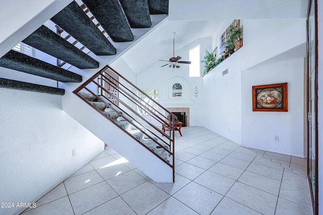 stairway with ceiling fan, tile patterned flooring, high vaulted ceiling, and a tile fireplace