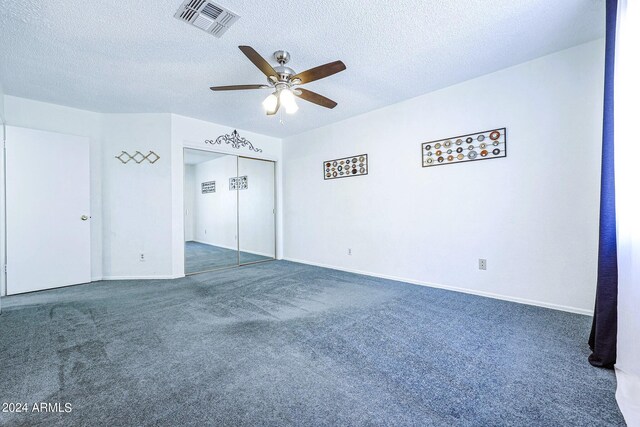 unfurnished bedroom with a textured ceiling, dark carpet, ceiling fan, and a closet