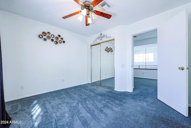 unfurnished bedroom with a textured ceiling, dark carpet, ceiling fan, and a closet