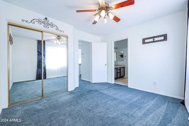 unfurnished bedroom with a closet, a textured ceiling, dark colored carpet, ceiling fan, and ensuite bathroom