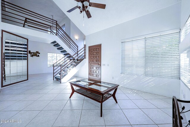 living room featuring a high ceiling, ceiling fan, light tile patterned floors, and a textured ceiling