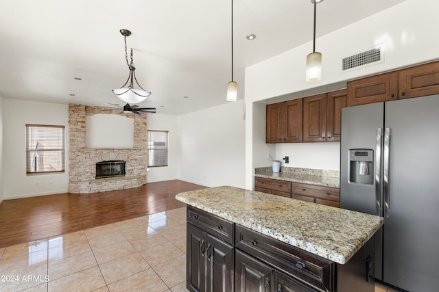 kitchen featuring a stone fireplace, stainless steel refrigerator with ice dispenser, hanging light fixtures, light hardwood / wood-style flooring, and ceiling fan