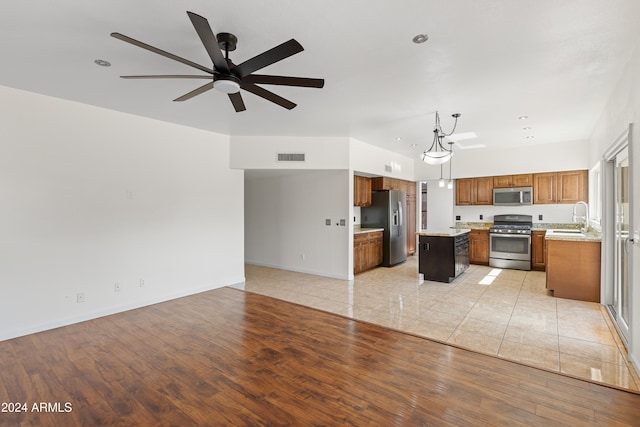 kitchen with a center island, hanging light fixtures, ceiling fan, appliances with stainless steel finishes, and light hardwood / wood-style floors