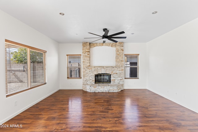 unfurnished living room featuring ceiling fan, a stone fireplace, and dark hardwood / wood-style flooring