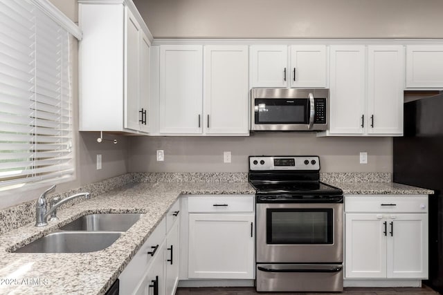 kitchen with stainless steel appliances, white cabinets, a sink, and light stone counters