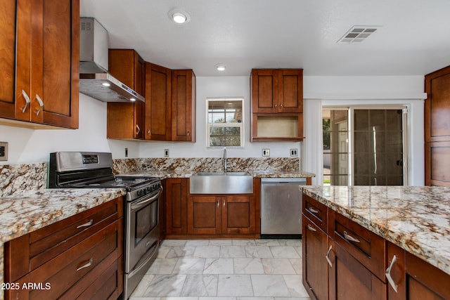 kitchen featuring light stone counters, visible vents, a sink, stainless steel appliances, and wall chimney range hood