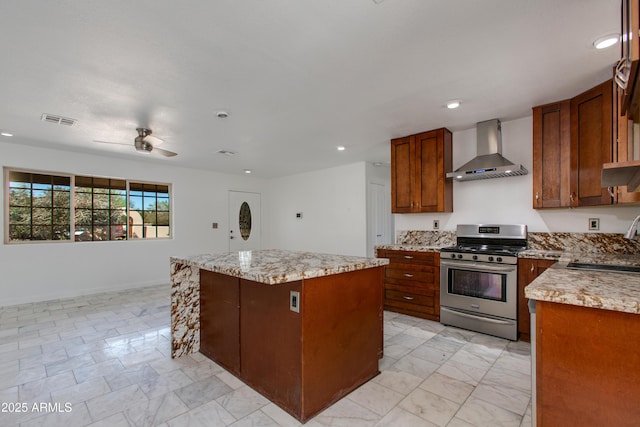 kitchen featuring stainless steel gas range oven, visible vents, a kitchen island, wall chimney range hood, and a sink