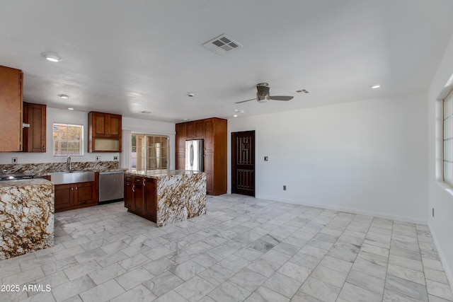 kitchen featuring visible vents, a kitchen island, light stone counters, stainless steel appliances, and a sink