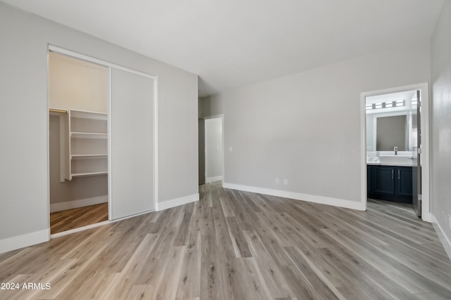 unfurnished bedroom featuring light hardwood / wood-style floors, a spacious closet, ensuite bath, and a closet