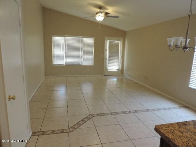 spare room featuring light tile patterned floors, baseboards, vaulted ceiling, and ceiling fan with notable chandelier