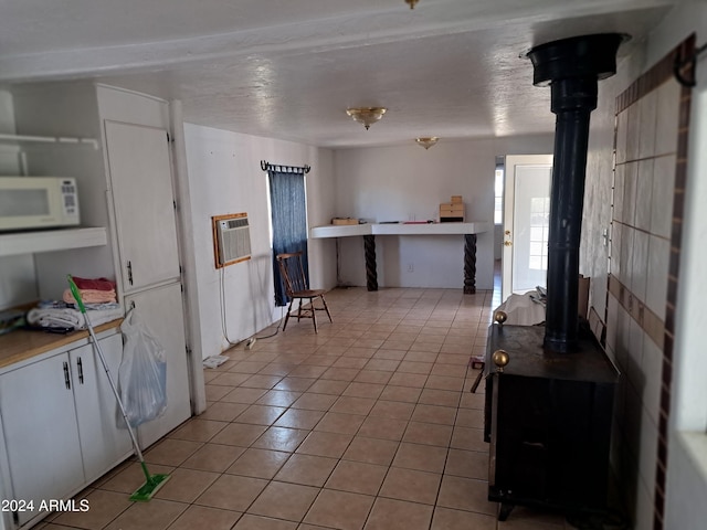 kitchen featuring a wood stove, white cabinetry, light tile patterned floors, and a wall mounted air conditioner