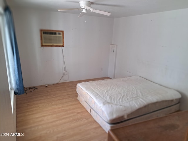 bedroom with ceiling fan, a wall mounted AC, and light hardwood / wood-style flooring