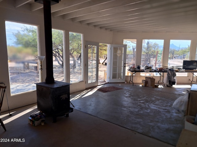 unfurnished sunroom with beamed ceiling and a wood stove