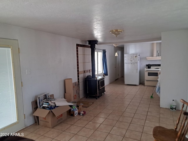 kitchen with a textured ceiling, a wood stove, light tile patterned floors, and white appliances