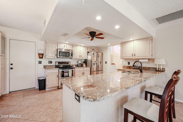 kitchen with kitchen peninsula, sink, a breakfast bar area, stainless steel appliances, and light stone counters