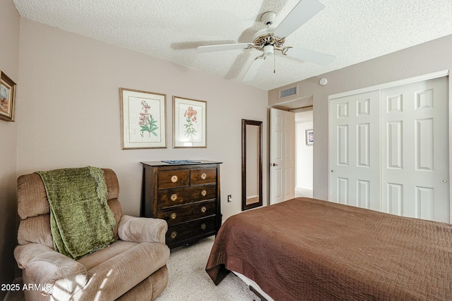 bedroom with a textured ceiling, ceiling fan, a closet, and light colored carpet