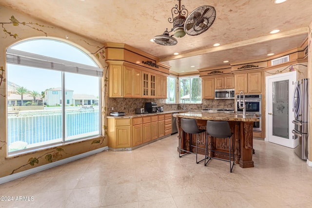 kitchen with appliances with stainless steel finishes, a kitchen island, a wealth of natural light, light stone countertops, and backsplash