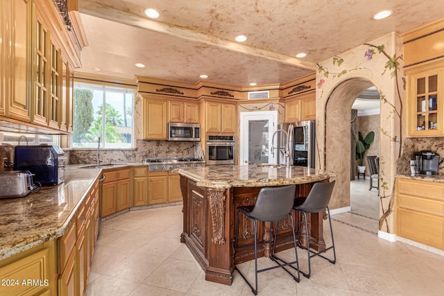 kitchen with sink, appliances with stainless steel finishes, light stone countertops, a center island with sink, and decorative backsplash