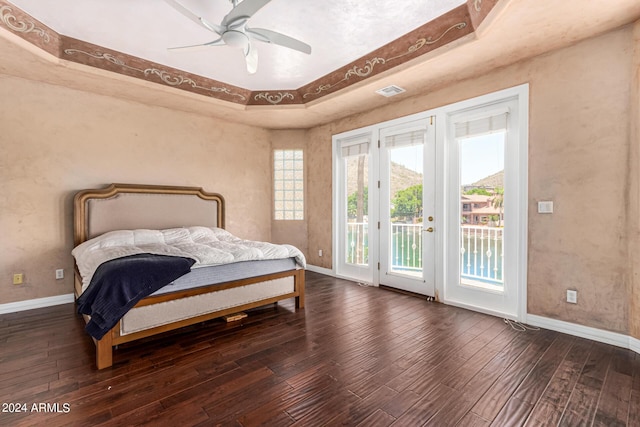 bedroom with access to exterior, a tray ceiling, hardwood / wood-style floors, and ceiling fan