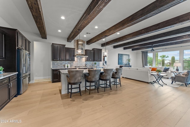 kitchen featuring wall chimney range hood, hanging light fixtures, stainless steel fridge, light hardwood / wood-style floors, and beamed ceiling