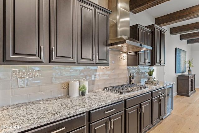 kitchen featuring wall chimney range hood, decorative backsplash, stainless steel gas stovetop, light wood-type flooring, and beamed ceiling