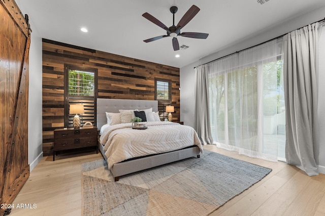 bedroom featuring light hardwood / wood-style flooring, wood walls, a barn door, and ceiling fan