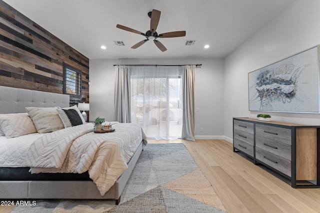 bedroom with ceiling fan, wood walls, and light hardwood / wood-style flooring