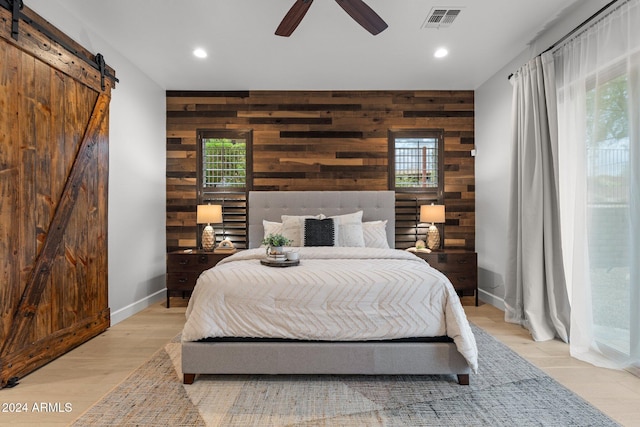 bedroom with light hardwood / wood-style floors, multiple windows, a barn door, and wooden walls