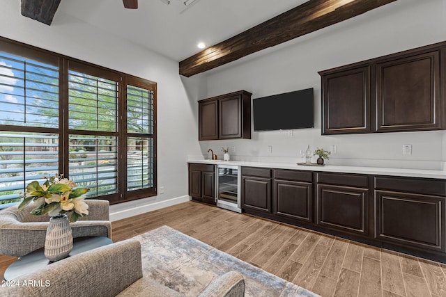 kitchen with dark brown cabinetry, light hardwood / wood-style flooring, beam ceiling, and beverage cooler