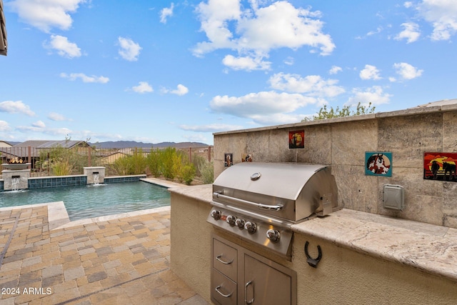 view of patio / terrace featuring pool water feature, a fenced in pool, a mountain view, an outdoor kitchen, and a grill