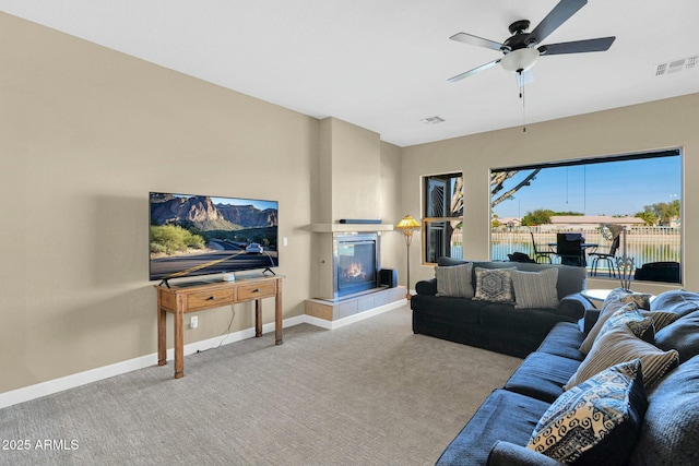 carpeted living room with a multi sided fireplace and ceiling fan