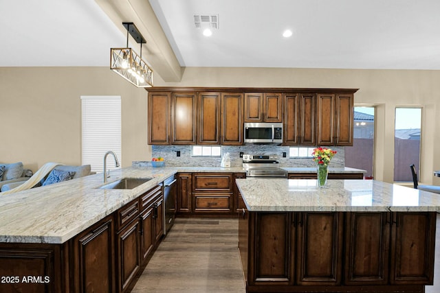 kitchen with sink, appliances with stainless steel finishes, decorative backsplash, decorative light fixtures, and kitchen peninsula