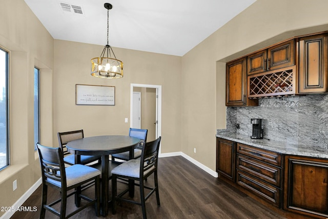 dining area featuring indoor bar, dark wood-type flooring, a notable chandelier, and plenty of natural light